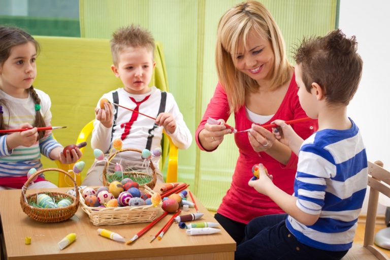 Young children painting Easter eggs with an art teacher